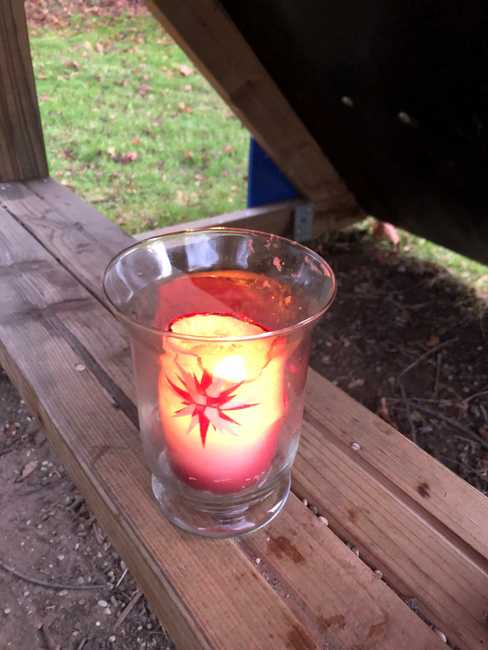 Eine brennende Kerze in einem Glas auf einer Spielplatz-Bank.