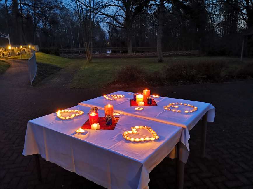 Ein Tisch, auf dem viele brennende Kerzen stehen; darunter Teelichter, die in Herzform angeordnet sind.
