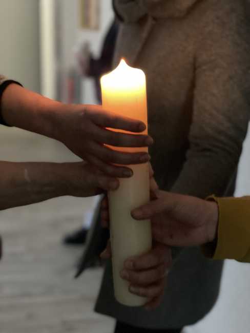 Mehrere Hände halten eine brennende Kerze.