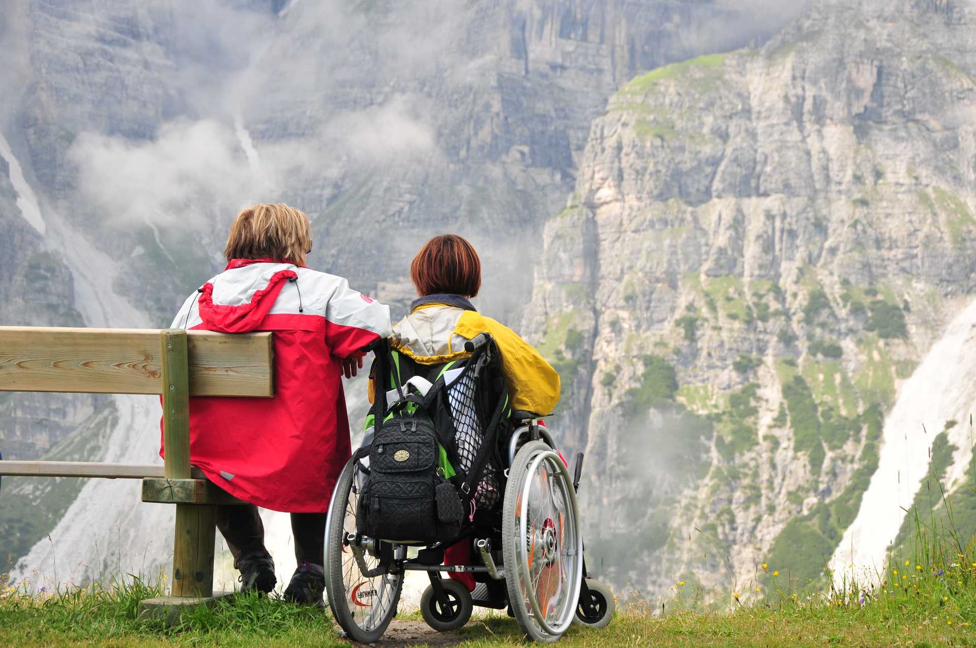 Zwei Frauen, eine im Rollstuhl, schauen auf ein Bergpanorama