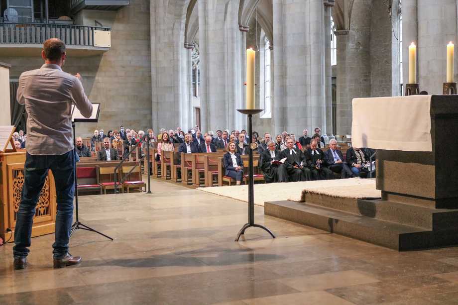 Ein Mann spielt Trompete in einer Kirche. In den Reihen sitzen viele Menschen.