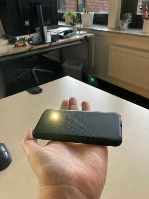 Auf einer ausgestreckten Hand liegt ein Smartphone. Die Rückseite zeigt nach oben, das Licht der Taschenlampe  leuchtet.