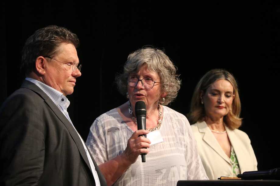 Zwei Frauen und ein Mann stehen mit einem Mikrofon am Podium