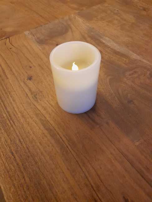 Eine elektrische Kerze steht auf einem Holztisch.