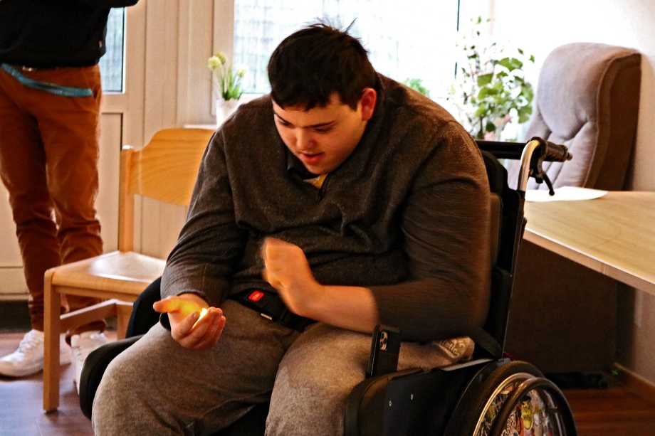 Ein Rollstuhlfahrer hält in seiner Hand ein leuchtendes, elektrisches Teelicht.